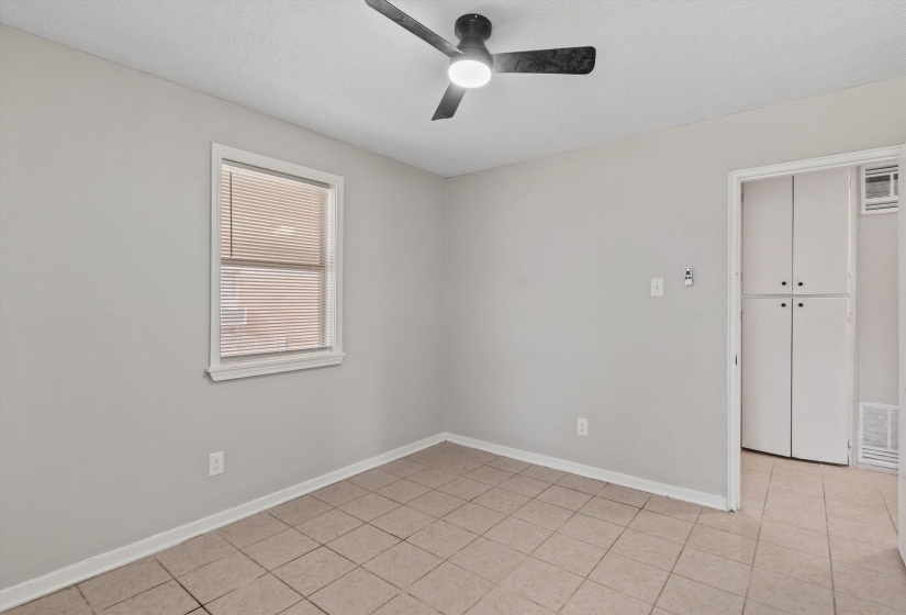 Neutral-toned room featuring a ceiling fan with integrated lighting, a window with horizontal blinds, tiled flooring, and a doorway opening to built-in white cabinetry