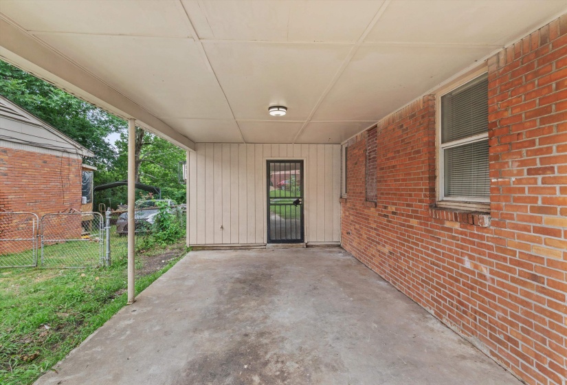 Covered carport featuring a concrete slab and exposed brick wall