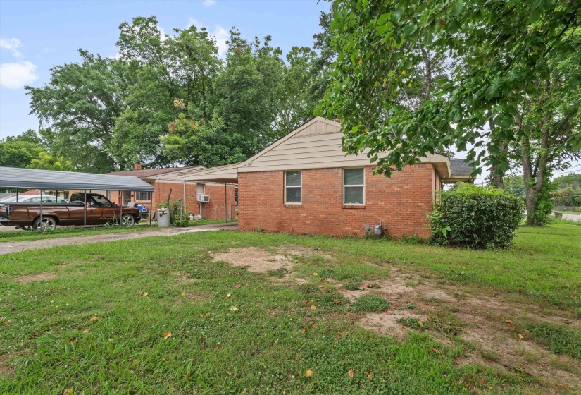 Brick exterior with tan siding and a covered carport, surrounded by mature trees