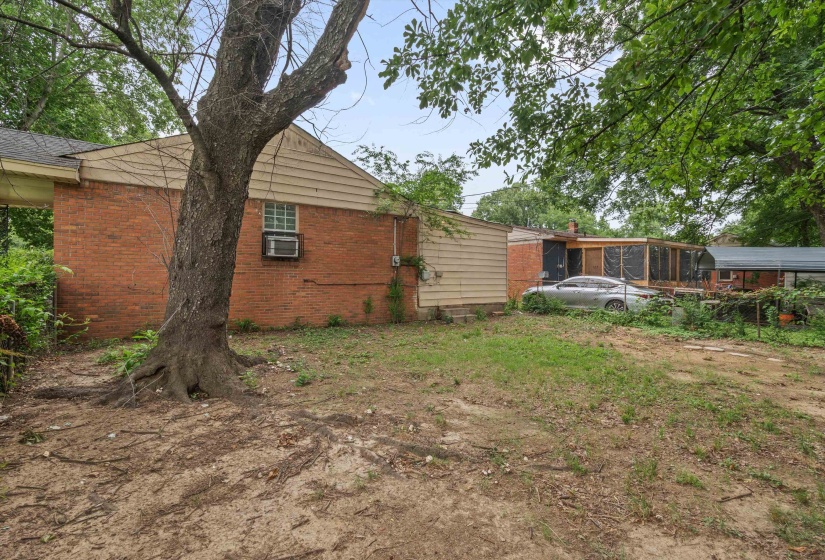Rear exterior featuring red brick siding with a horizontal panel accent, a mature shade tree, a screened-in structure, and a covered patio area