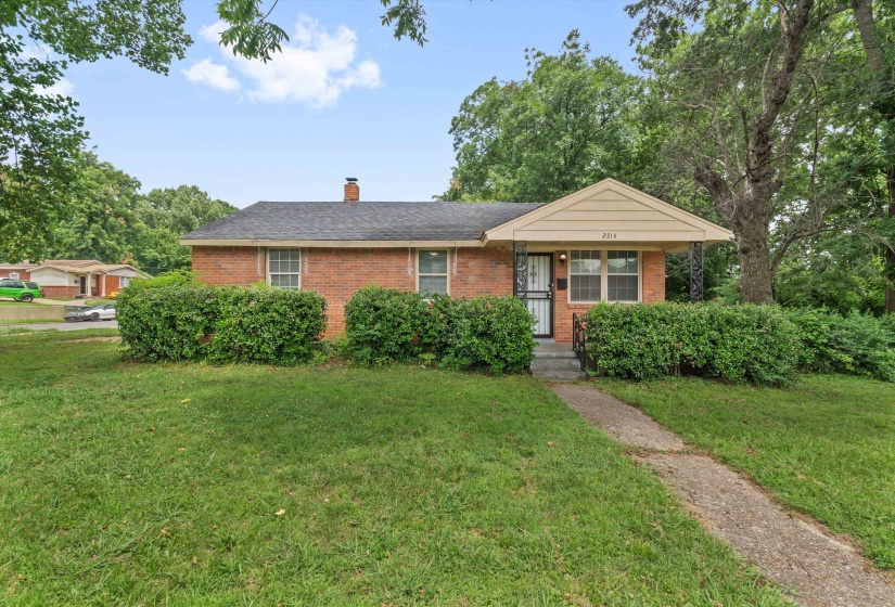 Brick ranch-style residence featuring a covered front porch with decorative wrought iron columns, a paved walkway, and a manicured front lawn with mature shrubbery