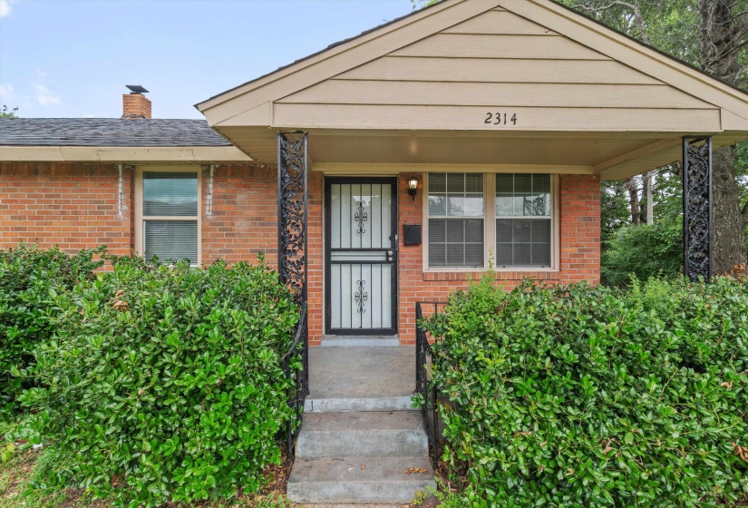 Brick exterior featuring a covered porch entry with decorative iron support columns and a dark security screen door