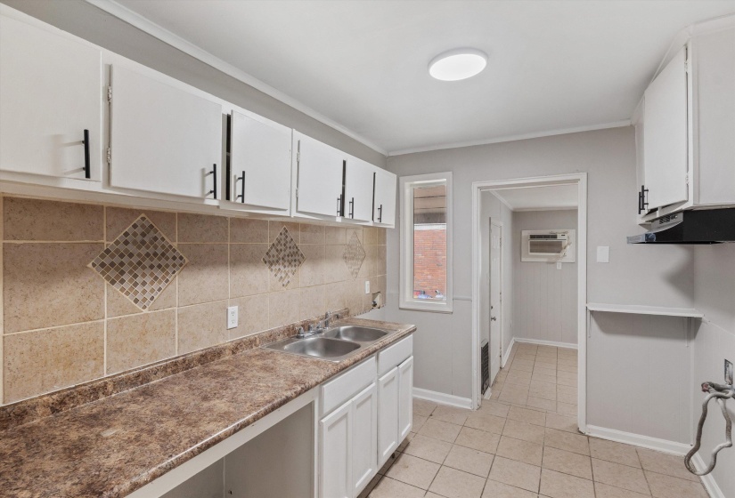 Kitchen featuring white cabinetry with black hardware, laminate countertops, a double basin stainless steel sink, and a tiled backsplash with mosaic accents