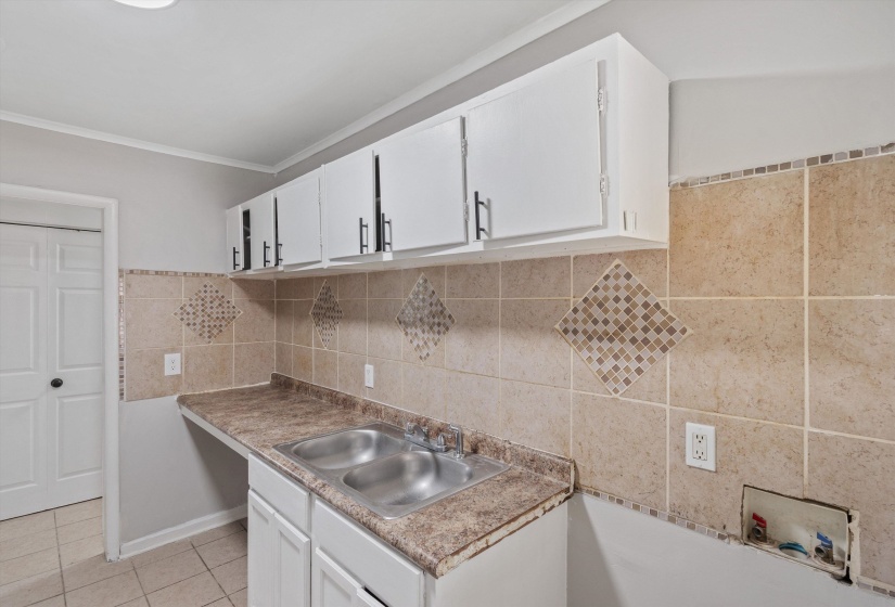 Utility space featuring a double basin stainless steel sink, laminate countertop, and tile backsplash with decorative mosaic accents