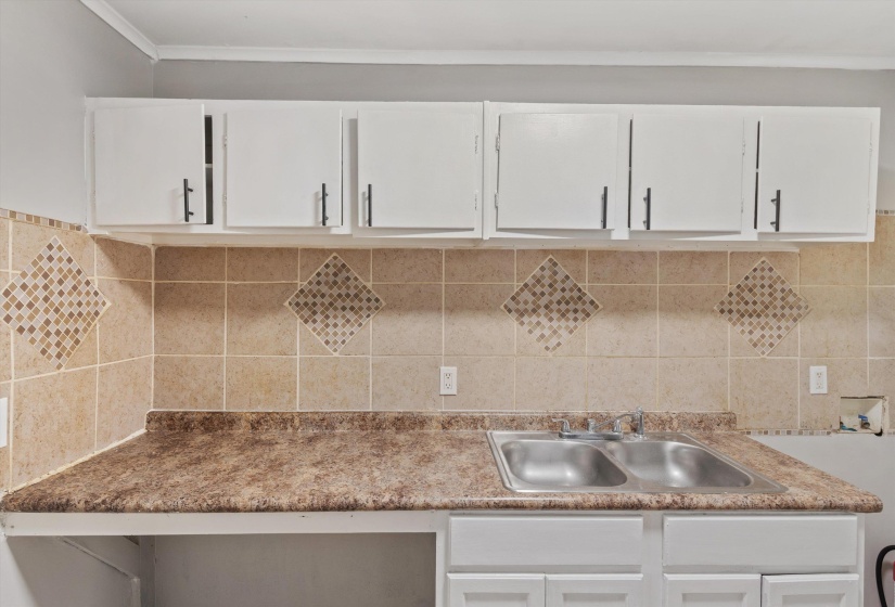 Kitchen featuring white upper and lower cabinetry, a double basin stainless steel sink, and a patterned tile backsplash