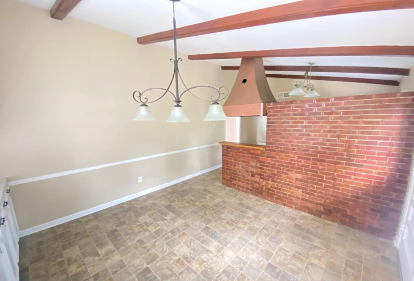 Interior space featuring a brick half-wall with a wood-finish bar top, exposed wood-beam ceiling, and patterned tile-look flooring