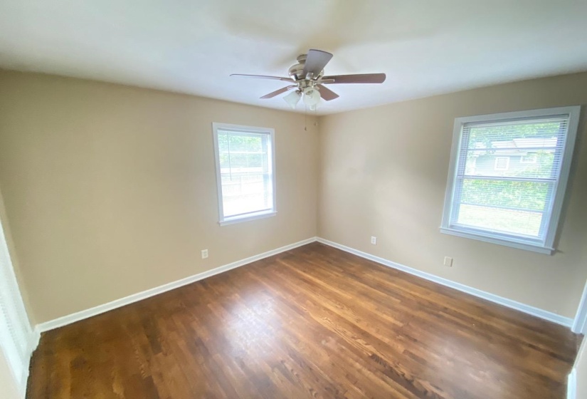 Hardwood flooring throughout, featuring two windows with white trim, a ceiling fan, and neutral-toned walls