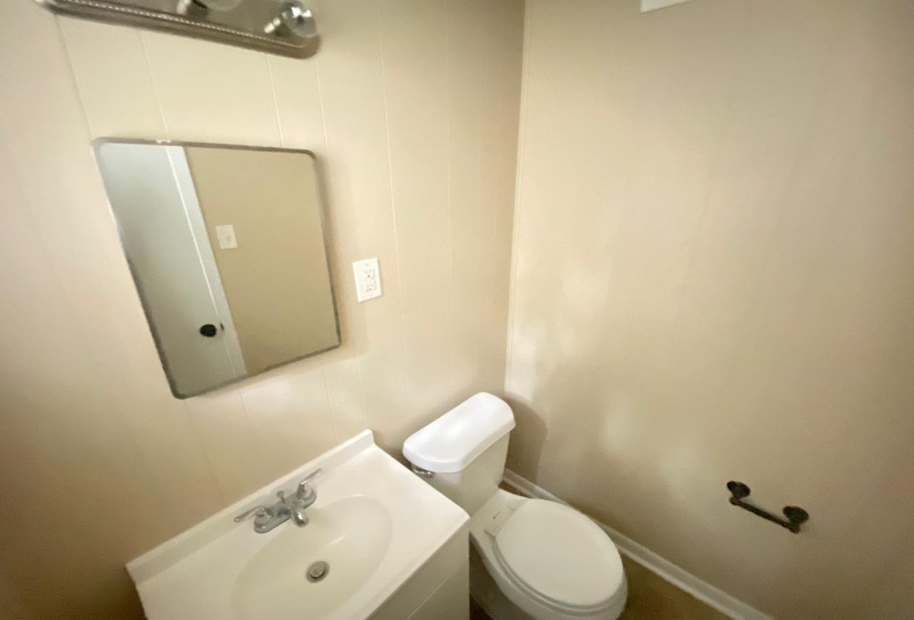 Bathroom featuring a white vanity with integrated sink, chrome faucet, rectangular wall mirror, and toilet