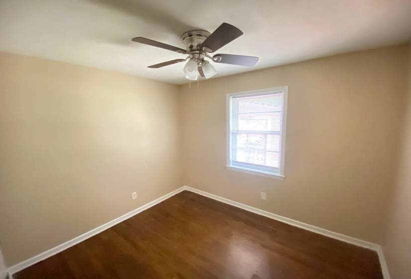 Room featuring wood-finish flooring, a ceiling fan with integrated lighting, a single window with blinds, and neutral wall tones