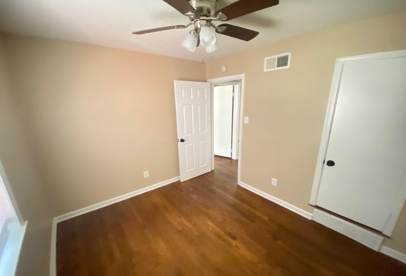 Room featuring wood-finish flooring, a neutral wall palette, white baseboards, a ceiling fan with light fixture, and a white paneled door