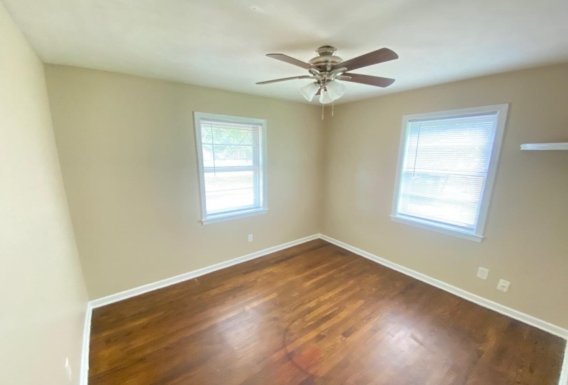 Interior room with wood-finish flooring, two large windows, a ceiling fan with integrated lighting, and neutral wall paint