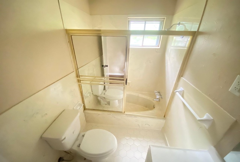 Bathroom featuring a tub/shower combination with sliding glass enclosure, hexagonal floor tiling, and a window for natural illumination