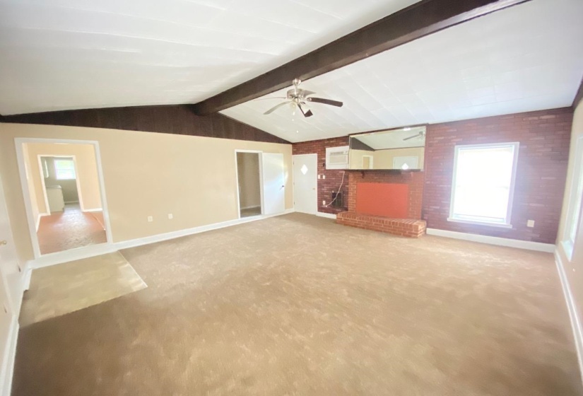 Spacious living area featuring a vaulted ceiling with exposed wood beams, a brick fireplace, and a ceiling fan