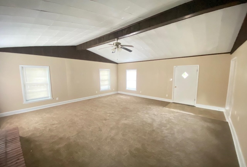 Spacious room featuring a vaulted ceiling with exposed beams, ceiling fan, and light-colored walls
