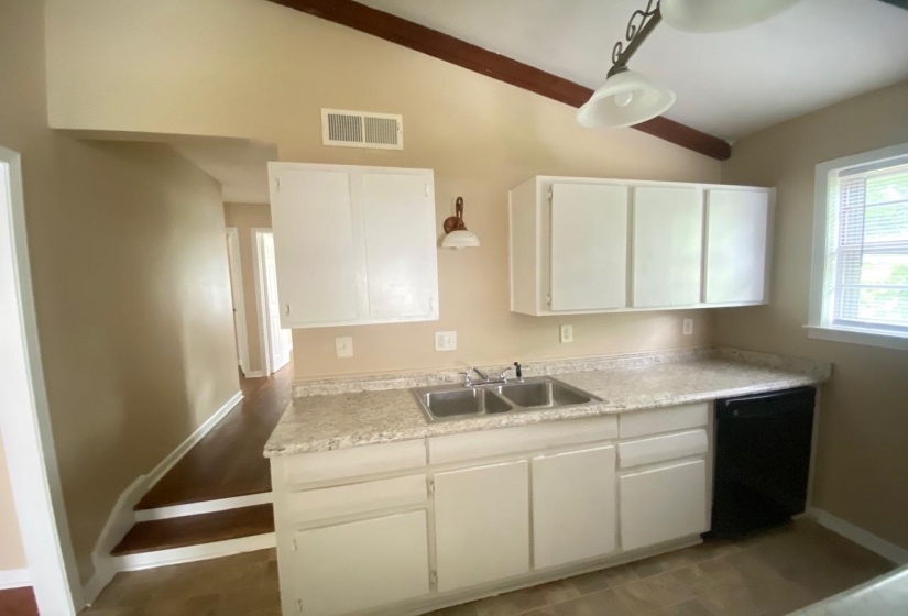 Kitchen area featuring white cabinetry, a double basin stainless steel sink, a black dishwasher, and speckled countertops