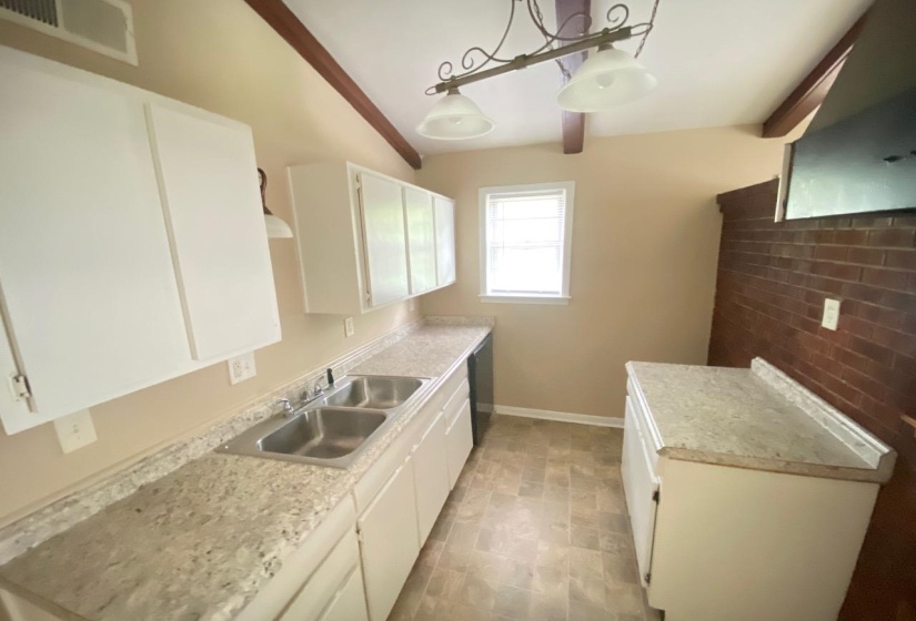 Kitchen featuring white cabinetry, light-colored countertops, a double basin stainless steel sink, a window with natural light, and exposed ceiling beams