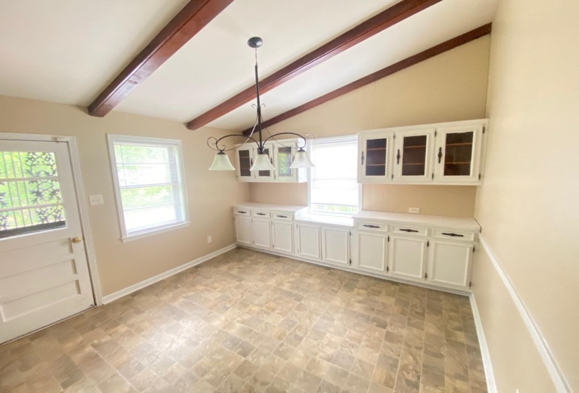 Vaulted ceilings with exposed wood beams define this space, featuring white cabinetry with glass-front uppers and white countertops