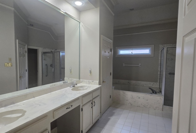 Spacious bathroom featuring a dual vanity with integrated sinks, a large wall-mounted mirror, a built-in bathtub with a tile surround, and a separate glass-enclosed shower