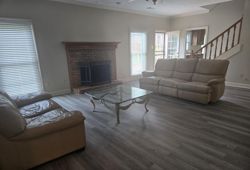 Spacious living area featuring a brick fireplace with a wood mantel, wood-finish flooring, and a multi-pane glass door leading to an outdoor area