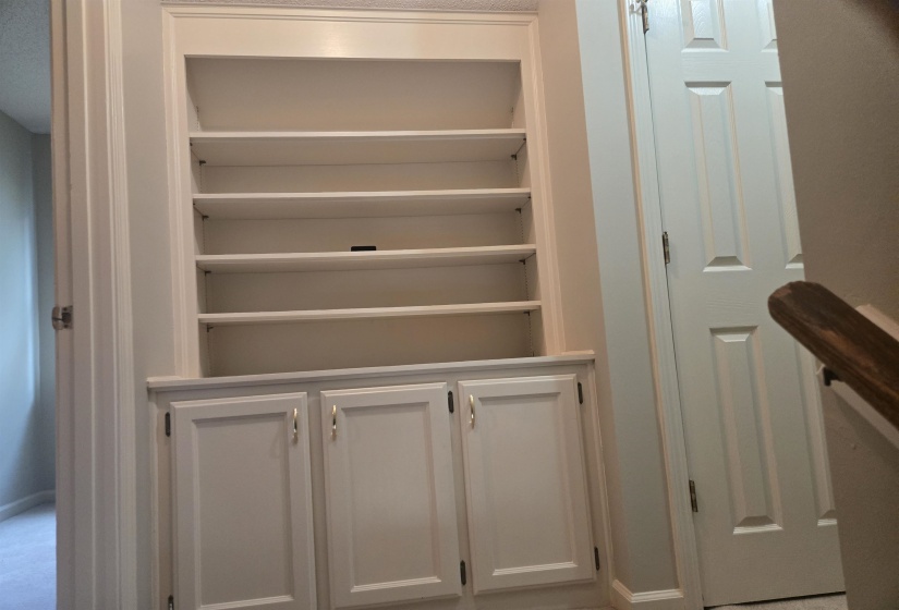 Built-in shelving unit with crown molding, adjustable upper shelves, and lower cabinet storage featuring polished brass hardware