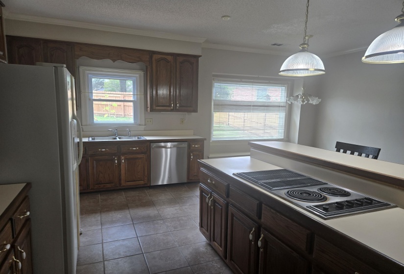 Kitchen featuring wood cabinetry, light-toned countertops, a built-in electric cooktop, stainless steel dishwasher, and tile flooring