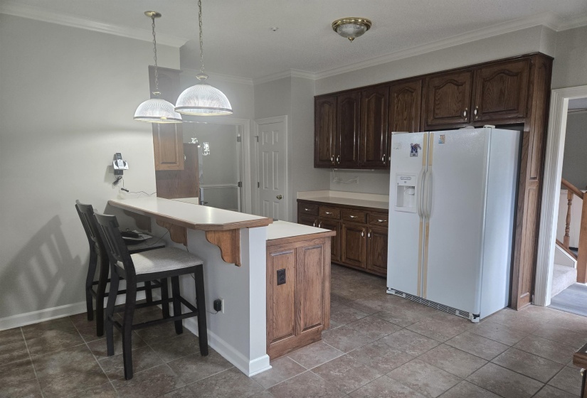 Kitchen featuring a breakfast bar with two pendant lights, wood-finish cabinetry, a white countertop, and tile flooring