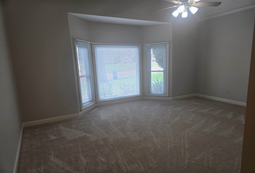 Bay window featuring three panels with blinds, carpet flooring, crown molding, and a ceiling fan with light fixture