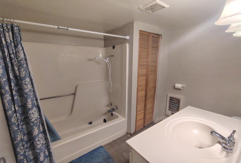 Bathroom featuring a white integrated sink vanity with chrome fixtures, a shower/tub combination with a grab bar, and louvered bifold closet doors