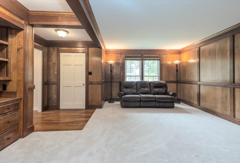 Room featuring extensive wood paneling and trim, built-in shelving, wood-finish flooring, and light-toned carpeting