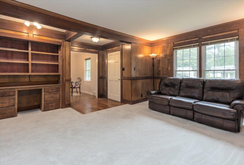 Spacious room featuring extensive wood paneling and trim, a built-in desk with shelving and drawers, multiple windows, and light-colored carpeting