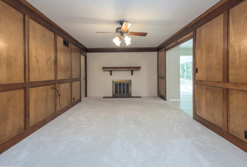 Spacious room featuring light-colored carpeting, a fireplace with a brass-toned insert and wood mantel, and a ceiling fan with integrated lighting