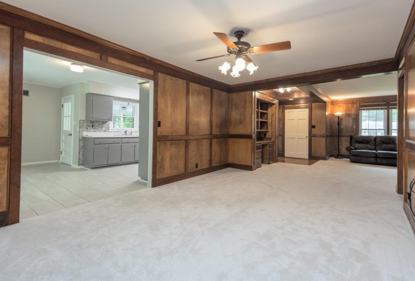 Spacious living area featuring light-toned carpeting and extensive wood paneling