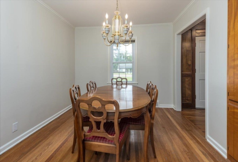 Dining area featuring wood-finish flooring, a window with exterior visibility, crown molding, and a chandelier