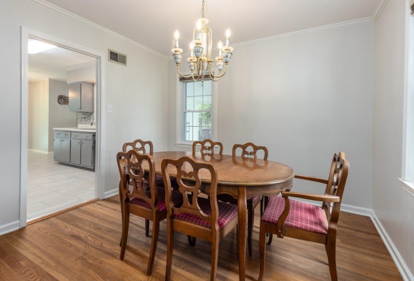 Dining area featuring wood-finish flooring, a brass chandelier, and crown molding
