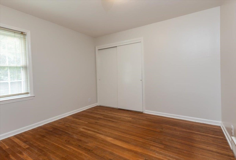 Bright interior space featuring wood-finish flooring, white baseboards, and a window with venetian blinds