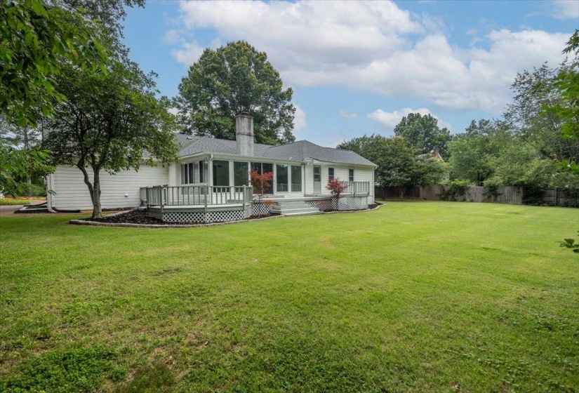 Expansive rear yard featuring a large green lawn, mature trees, and a multi-level wooden deck