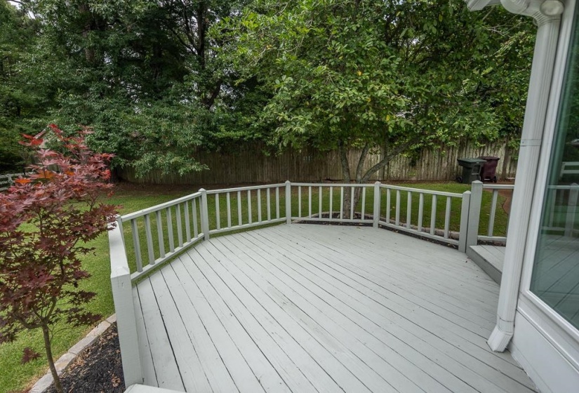 Spacious outdoor deck with painted wood railing overlooking a private backyard with mature trees