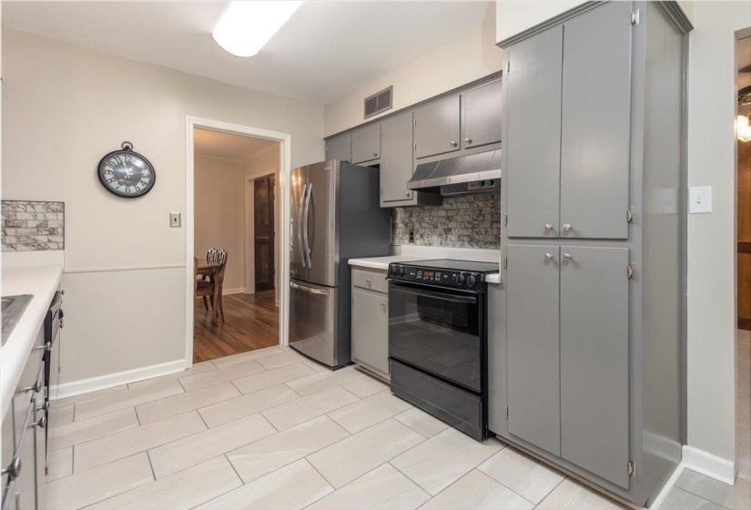 Kitchen featuring light-toned plank-style tile flooring, grey cabinetry with silver hardware, a black electric range, and a patterned tile backsplash