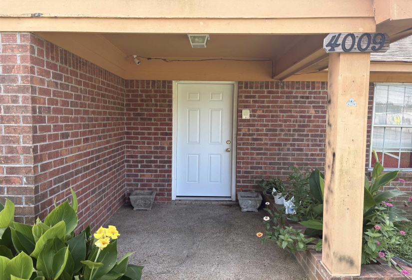 Covered entryway featuring a white paneled door, brick facade, and concrete porch