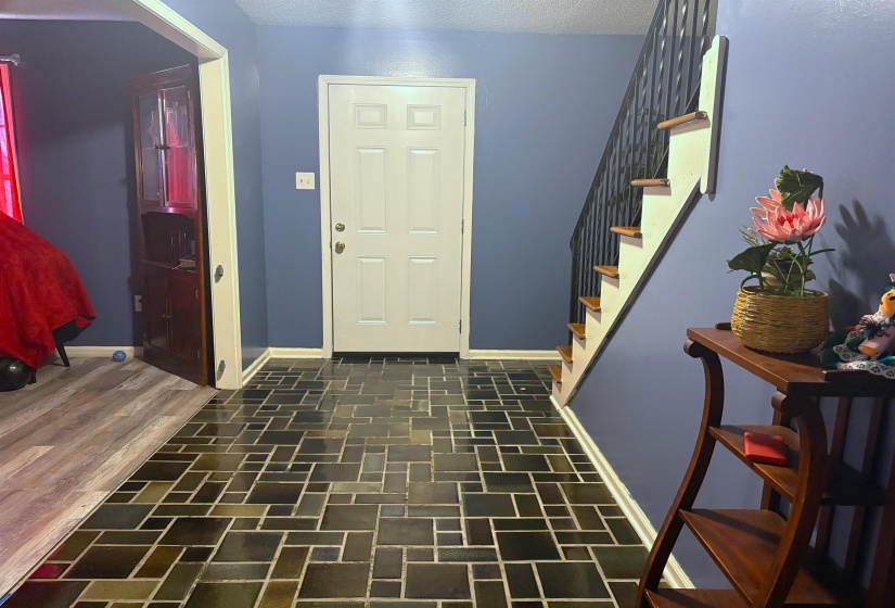 Entryway featuring patterned tile flooring, a white paneled door, and a staircase with wood treads and black metal balusters