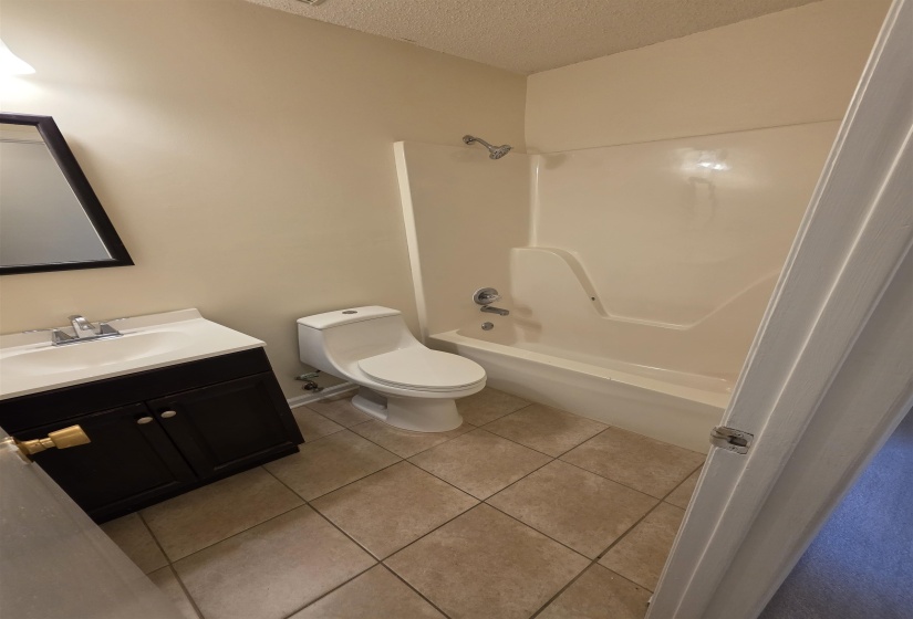 Bathroom featuring a tub/shower combination, dark wood-finish vanity with an integrated sink, polished chrome faucet, and tiled flooring