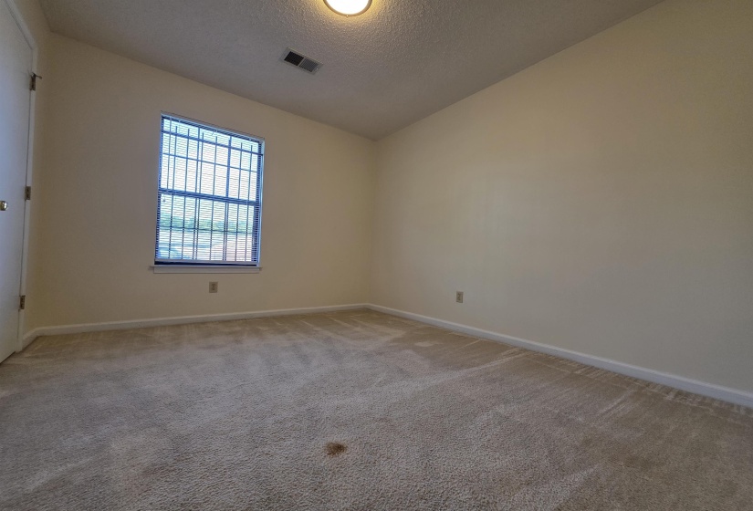 Carpeted interior room featuring a single window with security bars, vertical blinds, and light-toned walls