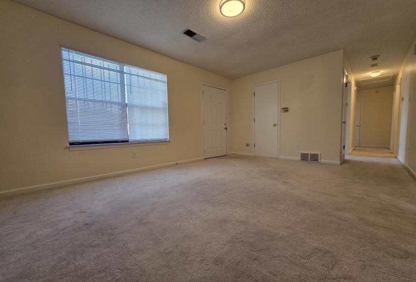 Carpeted room featuring a large window with blinds, two interior doors, and a hallway entrance