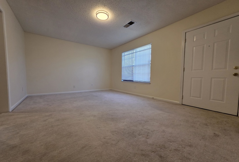 Carpeted room featuring a white paneled entry door with brass hardware, a window with horizontal blinds, a ceiling-mounted light fixture, and light-toned wall paint