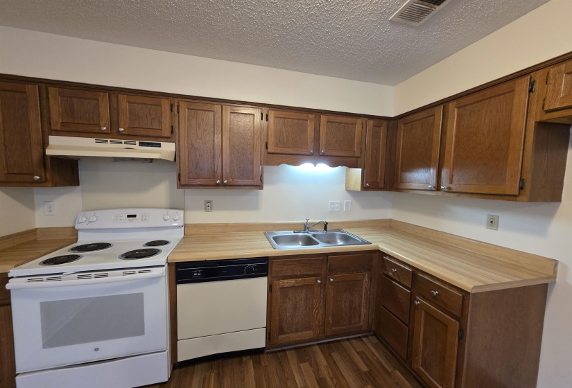 Kitchen featuring wood-finish flooring, wood cabinetry, laminate countertops, a double basin stainless steel sink, and white appliances including an electric range and dishwasher