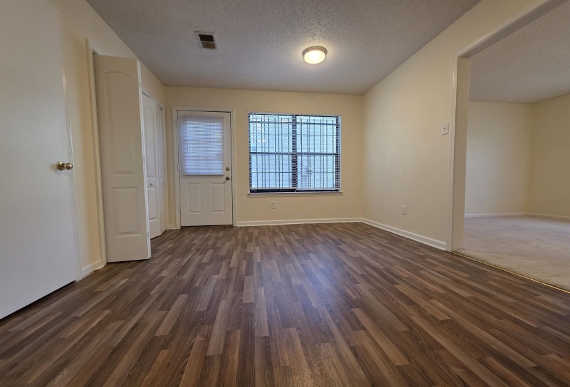 Spacious room featuring wood-finish flooring, light-colored walls, and a window with security bars