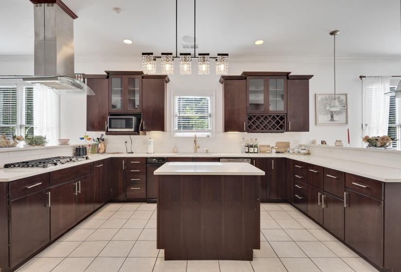 U-shaped kitchen featuring dark wood cabinetry, light countertops, a central island, stainless steel range hood, and tile flooring