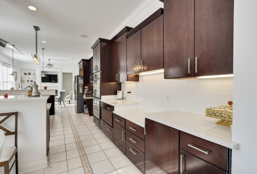 Kitchen featuring extensive dark wood cabinetry, white subway tile backsplash, light-toned countertops, and under-cabinet lighting