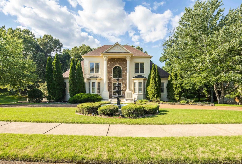 Stately stucco and stone exterior featuring a grand portico with columns, a prominent arched window, and a tiered fountain