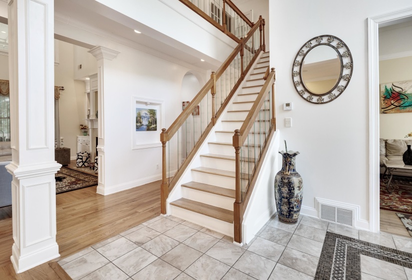 Two-story foyer featuring a staircase with wood handrails and balusters, tile flooring, and wood-finish flooring
